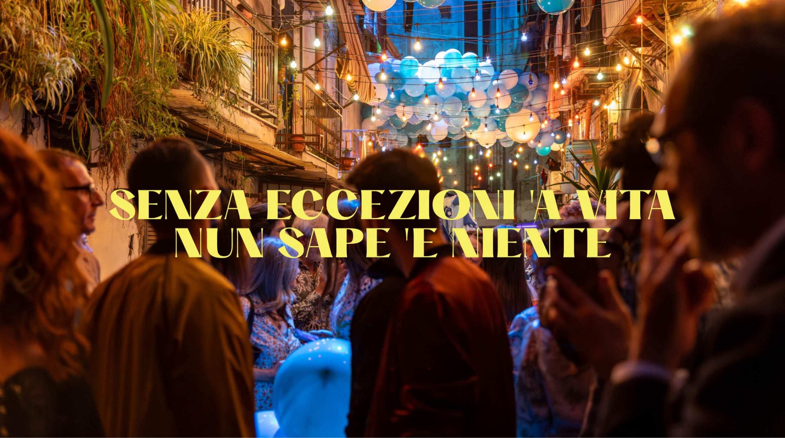 immagine senza eccezioni la vita non sa di niente. Testo giallo su sfondo sfocato raffigurante una festa di strada con palloncini e luci. | D SENZA ECCEZIONI A VITA NUN SAPE 'E NIENTE